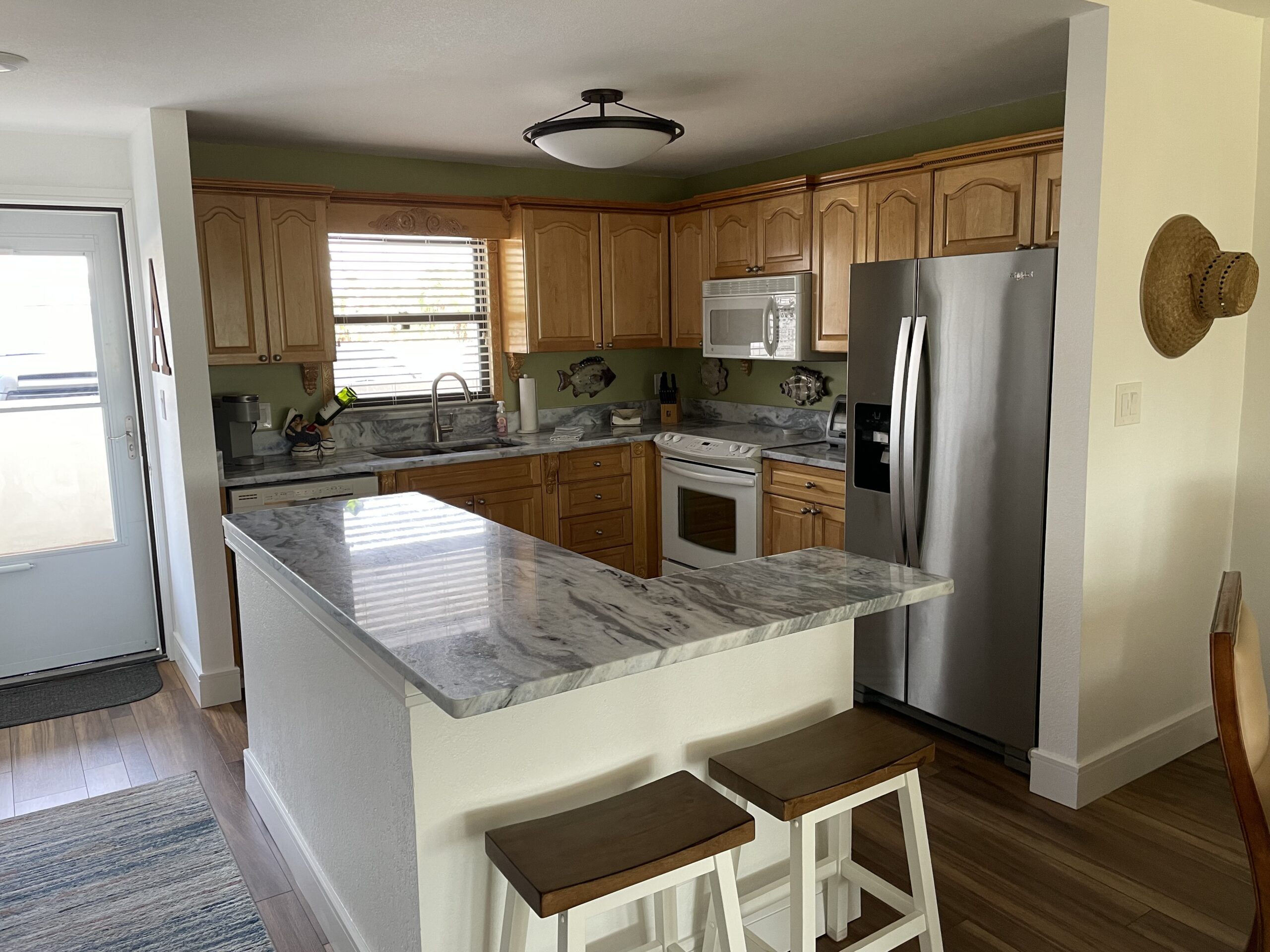 Bright full kitchen with breakfast bar, stainless fridge, and marble countertops in Sand Key Clearwater monthly condo rental